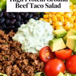 image of fresh ground beef romaine lettuce cherry tomatoes bell peppers black beans corn avocado cheddar cheese taco seasoning cilantro red onion lime juice Greek yogurt ranch seasoning salsa sour cream tortilla chips jalapeños arranged on white marble kitchen counter with clear glass bowls and rustic brown wooden kitchen sets under soft diffuse daylight