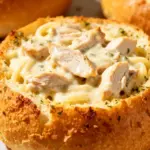 image of chicken breasts shredded chicken Italian French bread loaf baguette sourdough bread bowl Alfredo sauce base butter heavy cream Parmesan cheese garlic fresh minced garlic paste mozzarella cheese Parmesan cheese olive oil unsalted butter parsley fresh dried Italian seasoning poultry seasoning red pepper flakes Cajun creole seasoning salt black pepper onion powder garlic powder cream cheese basil additional fresh herbs extra shredded cheeses like provolone fontina marinara sauce for dipping additional red pepper flakes for heat extra Alfredo sauce for drizzling lemon zest or juice for brightness arranged on a white marble kitchen counter with healthy clear glass bowls and rustic brown wooden kitchen sets under soft diffuse daylight