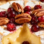 image of a top down mise en place shot showing a wheel of brie cheese whole berry cranberry sauce pecans brown sugar honey orange zest fresh rosemary and crostinis arranged on a white marble kitchen counter with healthy clear glass bowls and rustic brown wooden kitchen sets under soft diffuse daylight